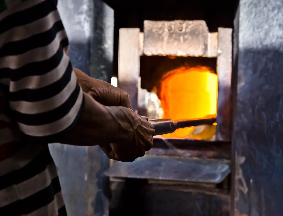 An artisan's hands working a blowpipe at the furnace